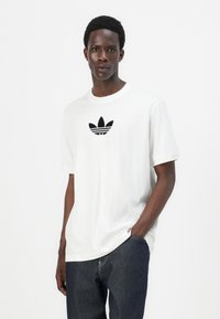 Witte katoen T-shirt met korte mouwen, voorzien van een zwart grafisch ontwerp van het adidas-logo op de borst. Ronde hals, ontspannen pasvorm.