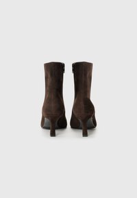 Bottines en suède marron avec un talon effilé, présentant une fermeture éclair à l'arrière et une texture lisse. Design classique, look polyvalent.