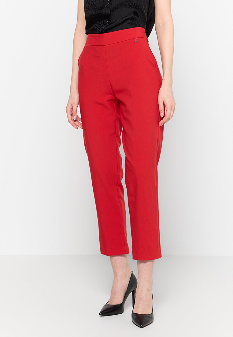 Donna con pantaloni alla caviglia rossi brillanti, tacchi a punta neri e un top senza maniche nero.