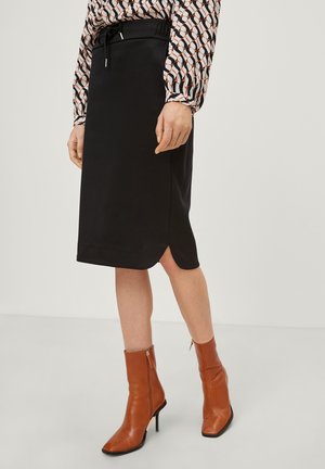 Black pencil skirt with an elastic waistband and drawstring. Features a slit at the hem. Worn with brown ankle boots.