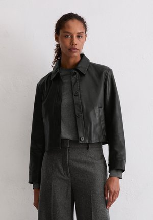 Schwarz lederne, taillierte Jacke mit spitzem Kragen, Knopfverschluss und Seitentaschen. Das Modell trägt einen grauen Pullover und maßgeschneiderte graue Hosen.