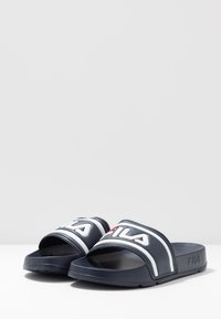 Mörkblåa sandaletter med bred rem som har vita och röda FILA-logotypdetaljer. Texturerad sula för grepp och komfort.