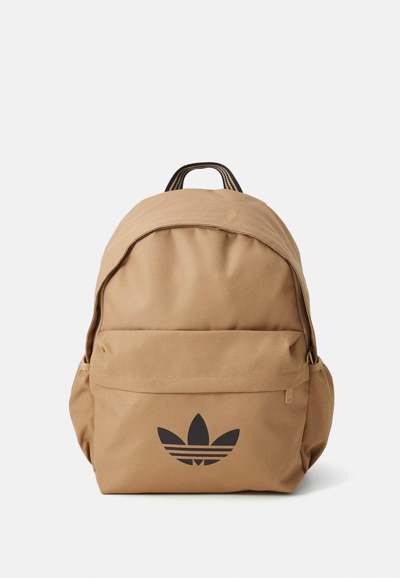 Mochila castanha feita de tecido resistente. Apresenta uma impressão de logotipo preto e um bolso frontal. Forma arredondada com uma pega superior e alças ajustáveis.