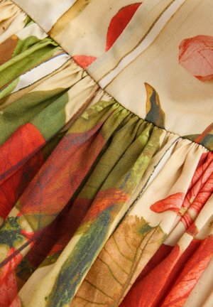 Gėlių raštas audinyje šiltais raudonos, žalios ir bežinės spalvų atspalviais, su plisuotais akcentais, pasižymintis švelnia tekstūra ir lengvu medžiagos svoriu.