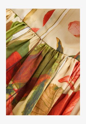 Gėlių raštas audinyje šiltais raudonos, žalios ir bežinės spalvų atspalviais, su plisuotais akcentais, pasižymintis švelnia tekstūra ir lengvu medžiagos svoriu.