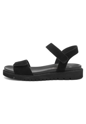 Schwarze flache Sandale mit dicker Sohle und verstellbaren Klettverschlüssen über den Zehen und um den Knöchel, Seitenansicht auf weißem Hintergrund.