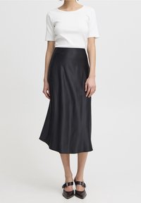 Musta satiininen midihame, jossa on sileä pinta ja hillitty kiilto, yhdistettynä tiukkaan valkoiseen ribattuun lyhythihaiseen toppiin ja kärjettiin mustiin kenkiin.