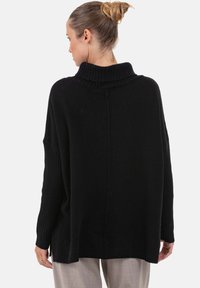 Pull noir surdimensionné avec un col montant côtelé, des épaules tombantes et des fentes latérales. Fabriqué en matière tricotée douce, avec une finition texturée.