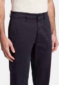 Granatowe bawełniane chinosy o prostym kroju nogawki, z zapięciem na guzik, paskiem i kieszeniami bocznymi. Gładka tekstura z minimalnymi detalami.