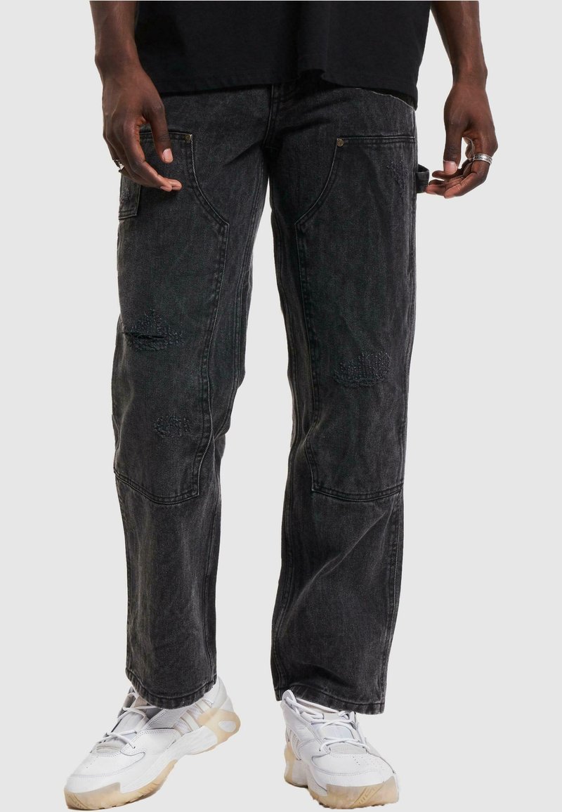 Black denim cargo pants featuring a relaxed fit, distressed accents, and multiple pockets. Worn with white sneakers for contrast.