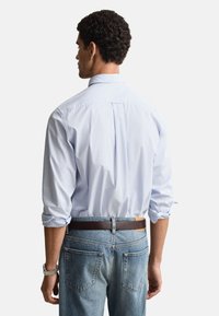 Hellblaues, langärmeliges Hemd mit Knöpfen, lockerer Schnitt, mit Rückenfalte und hochgekrempelten Ärmeln, kombiniert mit ausgewaschenen blauen Jeans und einem braunen Gürtel.