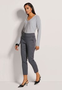 Lichtgrijze V-halstrui, gebloemde donkere broek en zwarte slingback hakken. De broek heeft een geometrisch patroon en een slim fit ontwerp.