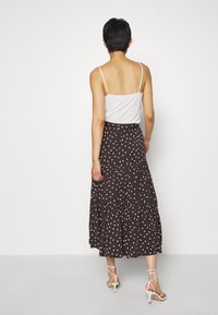 Bruine rok met polka dots en een gelaagd ontwerp, gemaakt van lichtgewicht stof. Gecombineerd met een wit spaghettihemd en witte sandalen met bandjes.