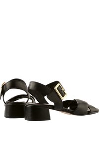 Černé kožené sandály s texturovaným povrchem, širokým páskem, zlatou sponou a nízkým blokovým podpatkem.