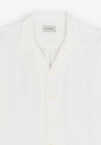 Camisa blanca de manga corta con cierre de botones en el frente, con textura de rayas verticales, un collar tipo camp y un material ligero y suave.