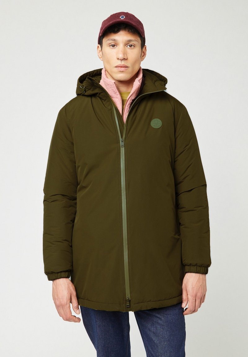 Gewatteerde olijfgroene parka met een ritssluiting aan de voorkant, een verstelbare capuchon, ribgebreide manchetten en een ronde embleem. Draagt over een roze fleece laag.