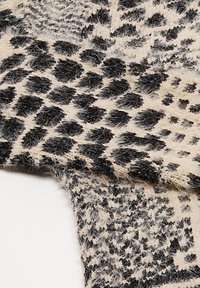 Tejido de punto que presenta un patrón de print animal en negro y beige, con una textura suave y peluda, que muestra formas y trazos variados.