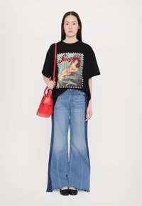 Camiseta negra de gran tamaño con un estampado gráfico, jeans anchos de color azul claro con paneles oscuros a los lados, y un bolso texturizado rojo. Bailarinas negras.