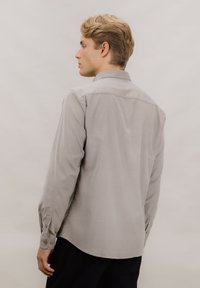 Grå skjorte med lange ermer, rett krage og en subtil teksturert stoff. Har avrundet kant og knapper ved mansjettene.