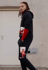 Casual black hoodie with red accents, featuring a graphic print. Paired with black sweatpants displaying a photo print on the pocket.