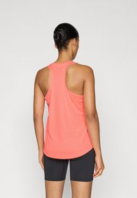 Κοραλί αμάνικη μπλούζα racerback από ελαφρύ ύφασμα, με ομαλή υφή και στρογγυλεμένο τελείωμα, συνδυασμένη με μαύρο σορτς.