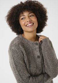 Texturerad grå cardigan med stora bruna knappar, rund halsringning och långa ärmar. Mjuk, varm material med en lös passform.