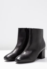 Schwarze Leder Stiefeletten mit abgerundetem Zehen, glatter Oberfläche, seitlichem Reißverschluss und robustem Blockabsatz.