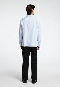 Ljusblå och vit randig långärmad skjorta med ryggsöm, ihopparad med svarta rakbenade byxor och kraftiga svarta skor.