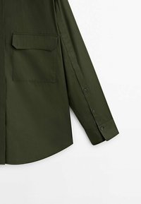 Chemise à manches longues vert olive en coton lisse. Elle présente une poche plaquée et des poignets boutonnés, avec une coupe ajustée et un ourlet arrondi.