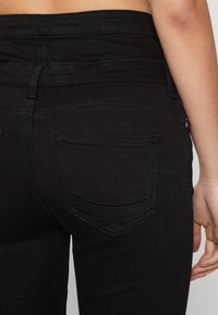 Jeans negros de cintura alta con una textura de tela suave, que presentan dos bolsillos traseros y sutiles detalles de costura.