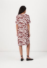 Robe rouge et blanche longueur genoux avec des manches courtes, ornée d'un motif floral et à coupe droite. Associée à des chaussures plates noires à lanières.