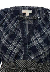 Tengerészkék kockás ruha fehér kockás mintával, rugalmas nyakkivágással és masnival. Vágott nyakkivágást és texturált szöveti részleteket tartalmaz.