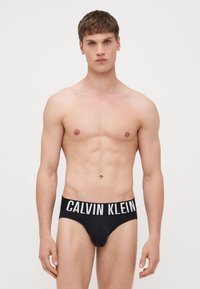 Culotte en coton noir avec une large ceinture élastique ornée du logo "CALVIN KLEIN" en blanc. Design ajusté qui souligne la silhouette. Texture lisse.