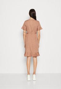 Vestido marrón con lunares, de mangas cortas, cintura ajustada y dobladillo con volantes. Hecho de una tela suave, presenta un diseño fluido y una textura delicada.