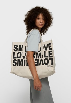 Bolsa grande de lona en color crema con texto negro en negrita: "SMILE LOVE" y "SMILE." Cuenta con asas resistentes y un interior espacioso.