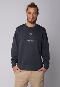 Donkergrijze sweatshirt met lange mouwen, ronde halslijn en een grafische afdruk van een figuur met een boom op de horizon. Zachte textuur.