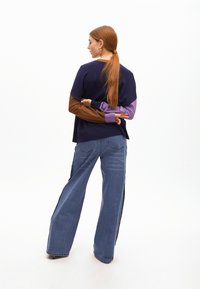 Wielokolorowy sweter z długimi brązowymi, fioletowymi i granatowymi rękawami, zestawiony z szerokimi niebieskimi dżinsami o efekcie postrzępienia, posiadającymi tylne kieszenie.