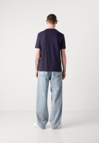 Marineblauwe katoenen t-shirt met korte mouwen en ronde hals, gecombineerd met lichtblauwe, wijde denim jeans. Glad materiaal, ontspannen pasvorm.