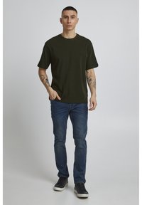 Oliven grøn bomulds t-shirt med korte ærmer, parret med blå denim jeans og sorte sneakers. Casual pasform og enkelt design.