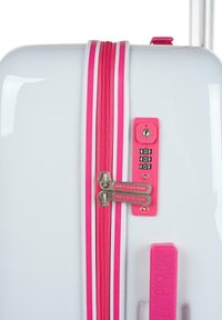 Maleta rígida blanca con un cierre rosa de doble cursor y una cerradura combinada, acentuada por rayas rosas en los laterales.