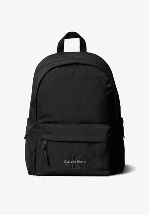 Sac à dos noir Calvin Klein avec poche zippée à l'avant et poignée supérieure, présenté sur fond blanc.