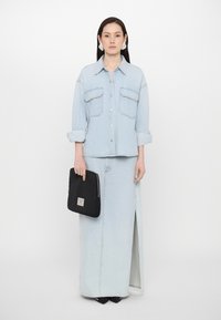 Camisa de mezclilla azul claro con dos bolsillos en el pecho, sin abotonar en el cuello, combinada con una larga falda de mezclilla azul claro que presenta una abertura lateral. Clutch negro con cremallera.