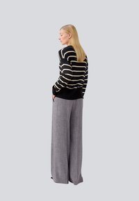Pull rayé noir et blanc, à manches longues, assorti à un pantalon large gris clair, avec un motif texturé subtil.