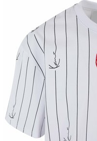 Vit kortärmad skjorta med vertikala svarta ränder, med en enkel grafisk tryck och röda accenter. Mjukt tyg med en slät textur.