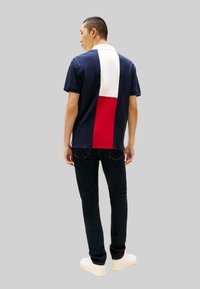 Marineblaues Poloshirt mit Color-Blocking-Design in Weiß und Rot; kombiniert mit dunklen Jeans und weißen Schuhen; Baumwollstoff.