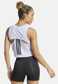 Witte cropped tanktop met uitsnijdingen, voorzien van drie zwarte verticale strepen op de rug. Gecombineerd met zwarte getailleerde shorts.