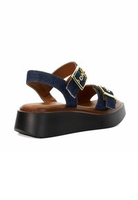 Blue denim platform sandal with two gold buckles, brown insole, and thick black sole, angled left on white background.