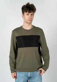 Sportswear verde oliva con un pannello in satin nero sul petto, scollo rotondo e maniche lunghe. Presenta un sottile logo dettagliato all'orlo.