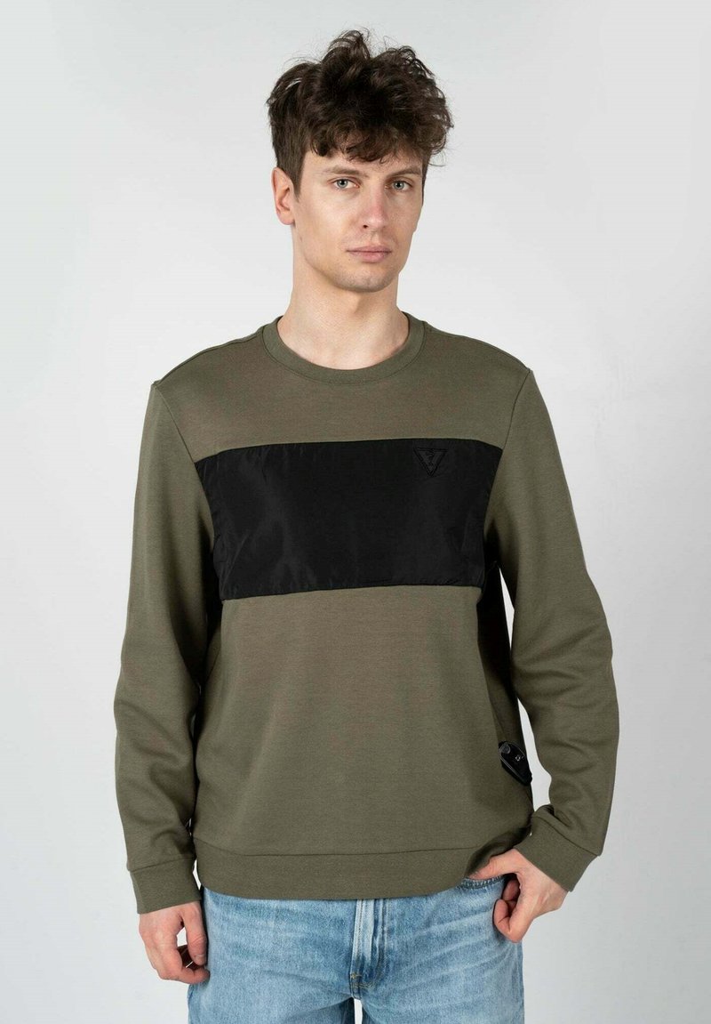 Sportswear verde oliva con un pannello in satin nero sul petto, scollo rotondo e maniche lunghe. Presenta un sottile logo dettagliato all'orlo.