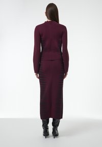 Bordeaux gebreide jurk met lange mouwen, geribbelde structuur en zwarte verticale strepen; beschikt over een hoge halslijn en een achterrits.